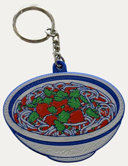 A flat keychain printed in layers showing a bowl of noodles with tomatoes and herbs, in full colour.